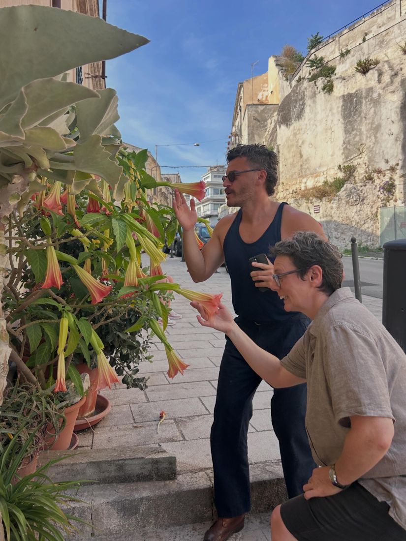 Two of the group stopping at angel's trumpet flowers on a street in Ortigia
