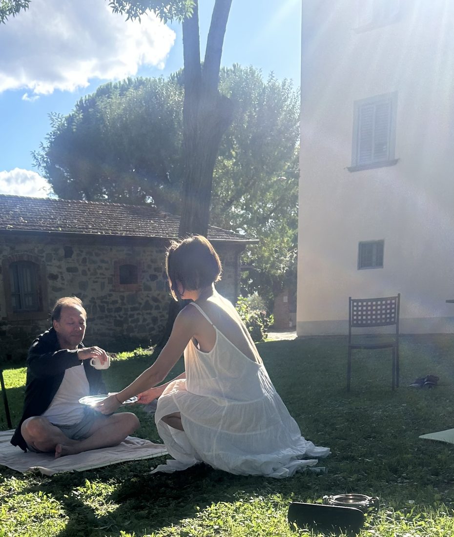 Tea passed between two participants on the grass in afternoon sun
